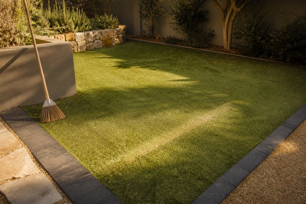 Mature artificial lawn showing sun fade and traffic wear in a Cape Town garden edged with paving brick