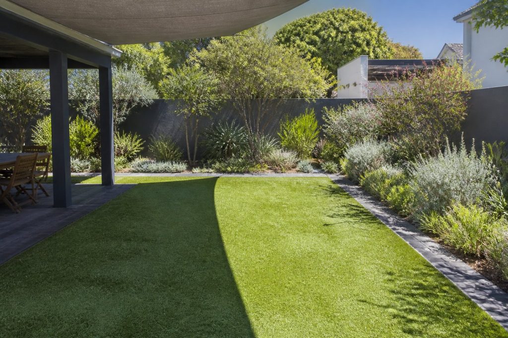 Artificial lawn half shaded by a shade sail and half in direct summer sun in a Cape Town back garden